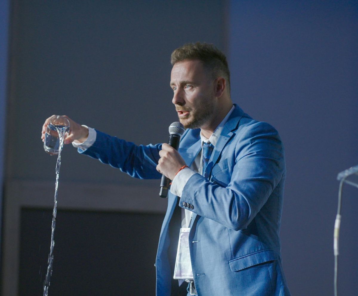Jorge Lago en el escenario, con micrófono, vaciando un vaso de agua mientras habla al público